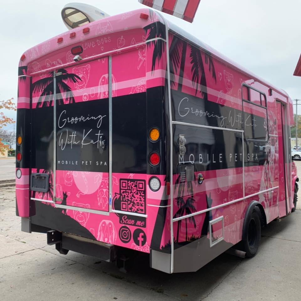 The back of a Grooming With Kate pink mobile pet spa bus
